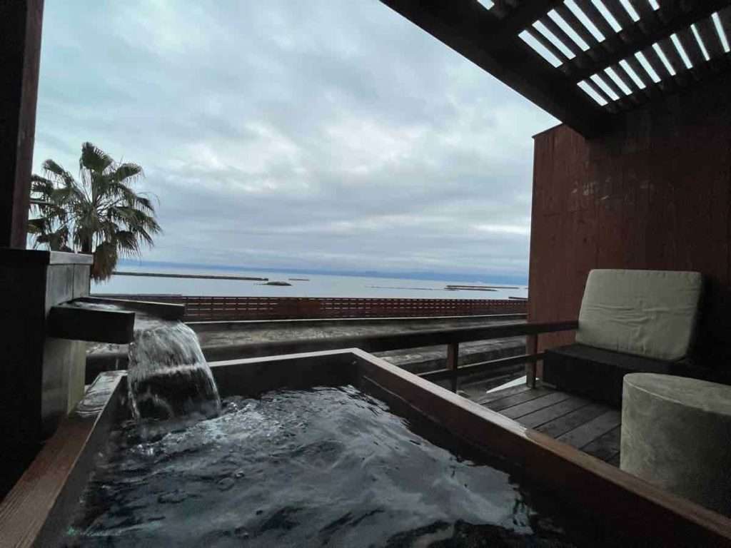 かけ流し温泉が流れ出すヒノキの客室露天風呂と鹿児島湾を望む景色