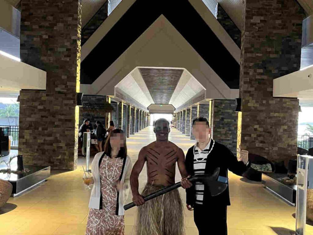 ホテルのエントランスで民族衣装を着たフィジアンと一緒に記念撮影する男女