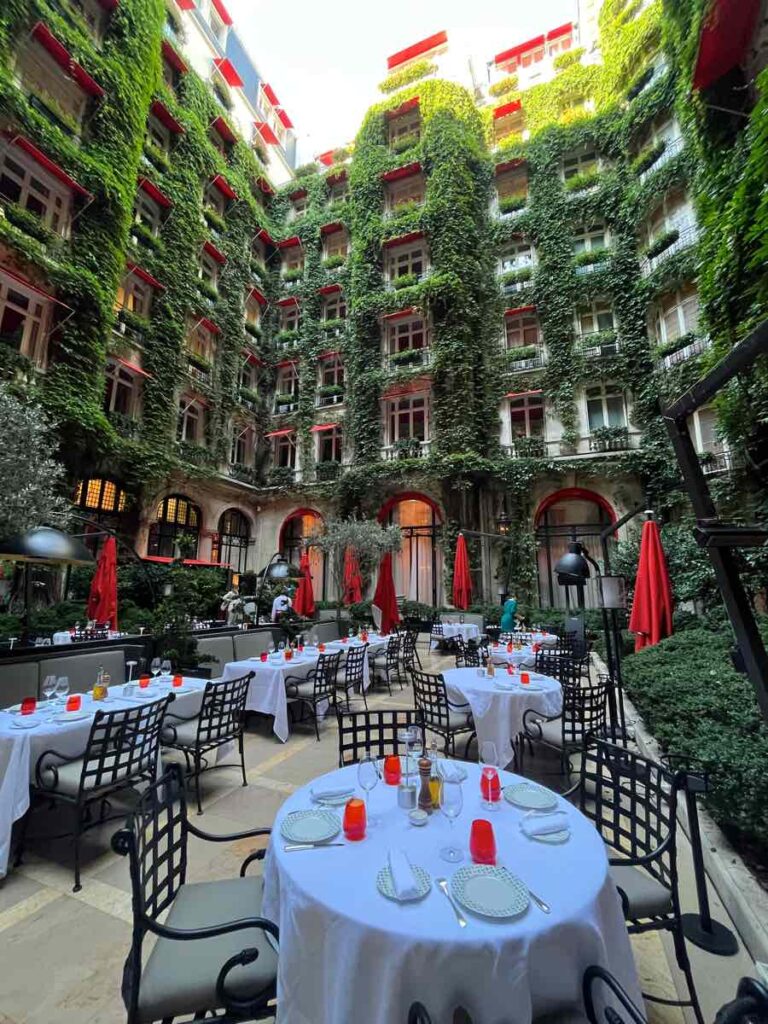白い壁と赤いテントにツタの植物が一面に生えているホテルの中庭(La Cour Jardin)