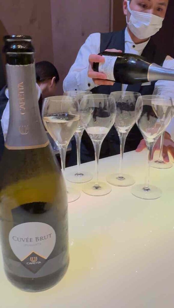 ワインのボトルと並べられたシャンパングラスにホテルの従業員がスパークリングワインを注いでいる