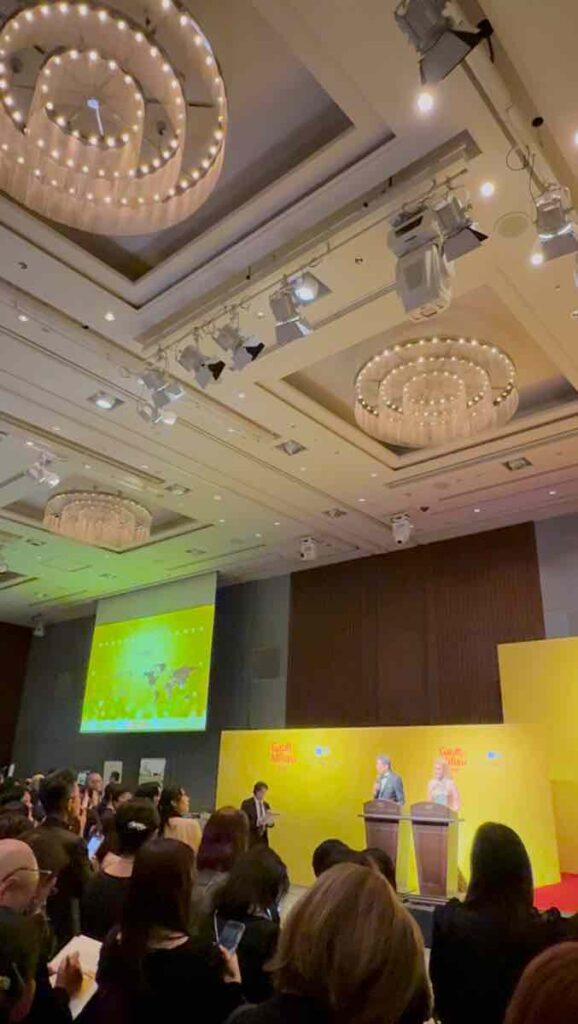 葵の間でにセットされた黄色い屏風の前で司会者が挨拶をしている