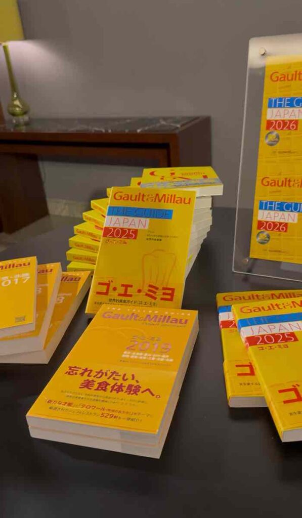 テーブルの上にゴ・エ・ミヨ2026と書いた黄色い表紙の美食のガイドブックが10数冊飾ってある